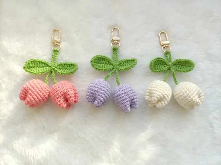 Three amigurumi keychain tulips in pink, purple, and white with green leaves on a white fuzzy background.