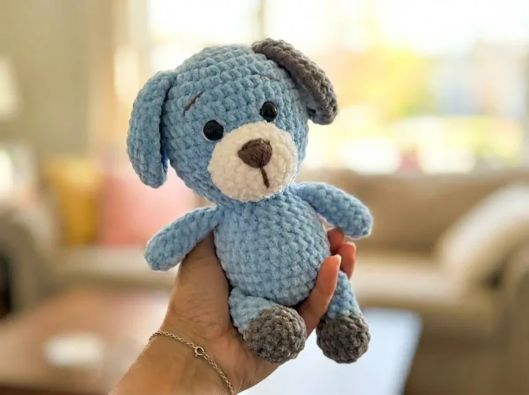 Plush crochet amigurumi dog Rex made with chenille yarn, sitting upright with cotton ear inserts and embroidered face details