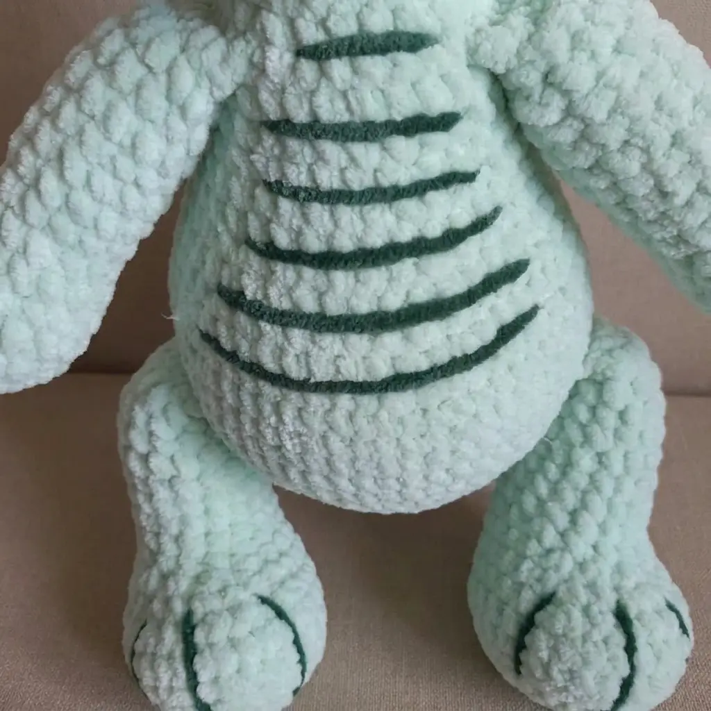 A detailed close-up of the plush dinosaur belly and claws, showing the striped pattern from this dino amigurumi free pattern on AmiLoops.com.