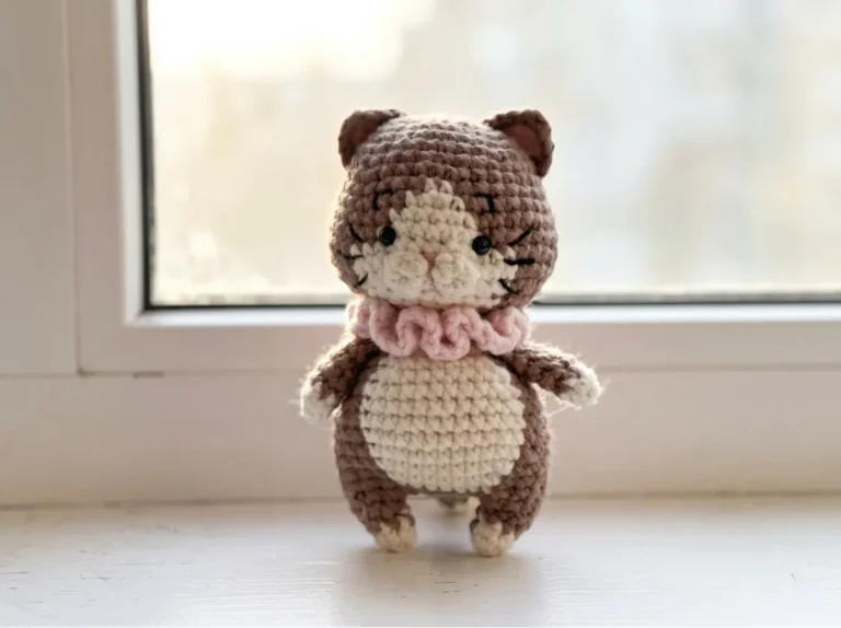 Brown and cream amigurumi cat with a pink collar on a bright windowsill from a cat crochet pattern free guide.