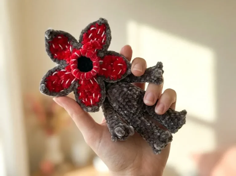 Hand holding a grey velvet crochet demogorgon free pattern toy with a red petaled face and white embroidered teeth.