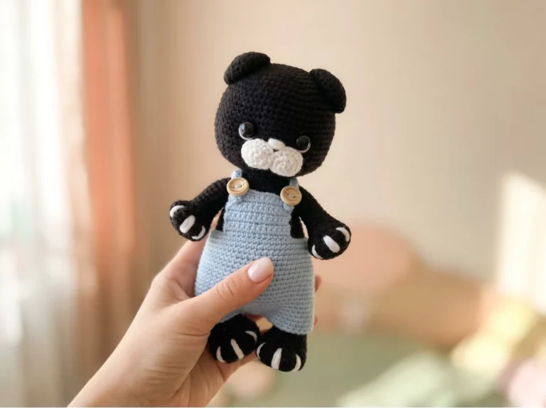 Hand holding a black amigurumi cat wearing blue overalls. Find this crochet kitten pattern free online.