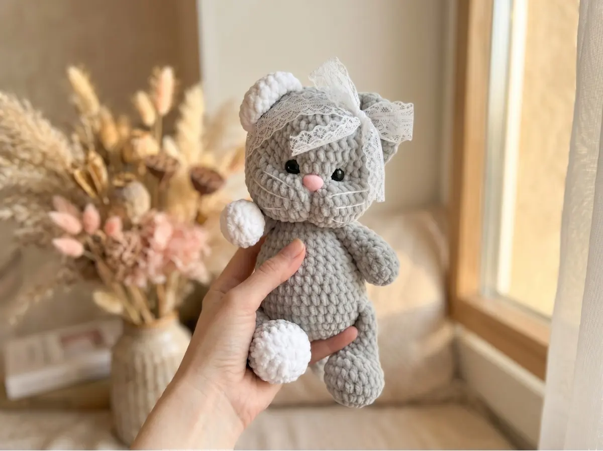 Grey plush yarn toy cat sitting held in hand, crafted with our crochet kitten pattern free tutorial.