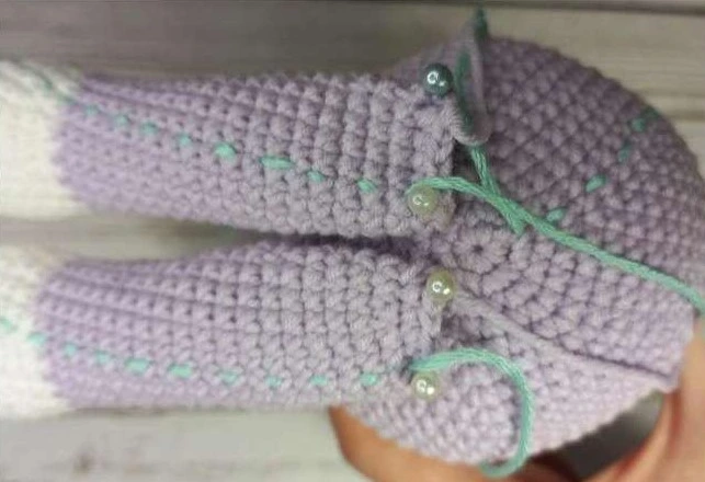 Close-up of two crocheted amigurumi unicorn legs with cream hooves pinned symmetrically to the bottom of a light lilac body piece using straight pins.