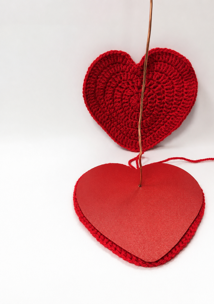 Finished red crocheted heart base with a yarn-wrapped wire stem topped by a small crocheted heart photo holder clip.