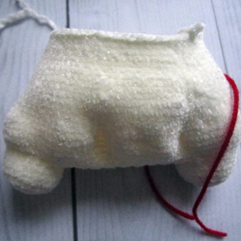Partially crocheted amigurumi unicorn body made of bulky white plush yarn, showing two legs at the base and the body building upwards, with a red yarn stitch marker on the right side.