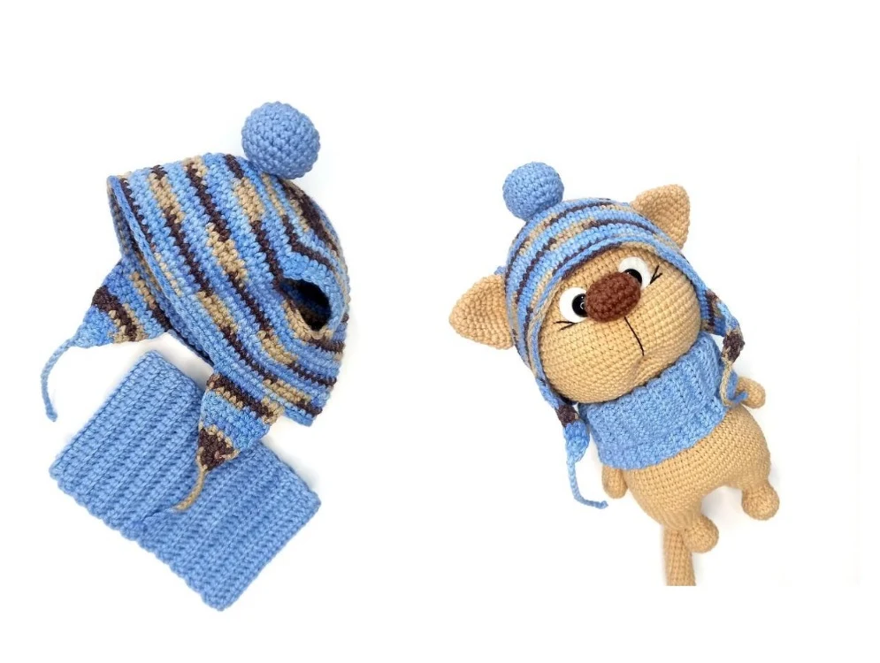 A striped blue, tan, and dark brown crocheted hat with ear holes, earflaps, and a top pompom, resting next to a matching solid light blue ribbed crocheted snood.