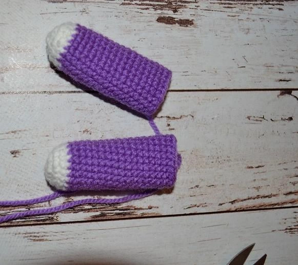 Two crocheted amigurumi unicorn legs resting on a rustic wooden surface, showing a clean color transition from white hooves to violet yarn.