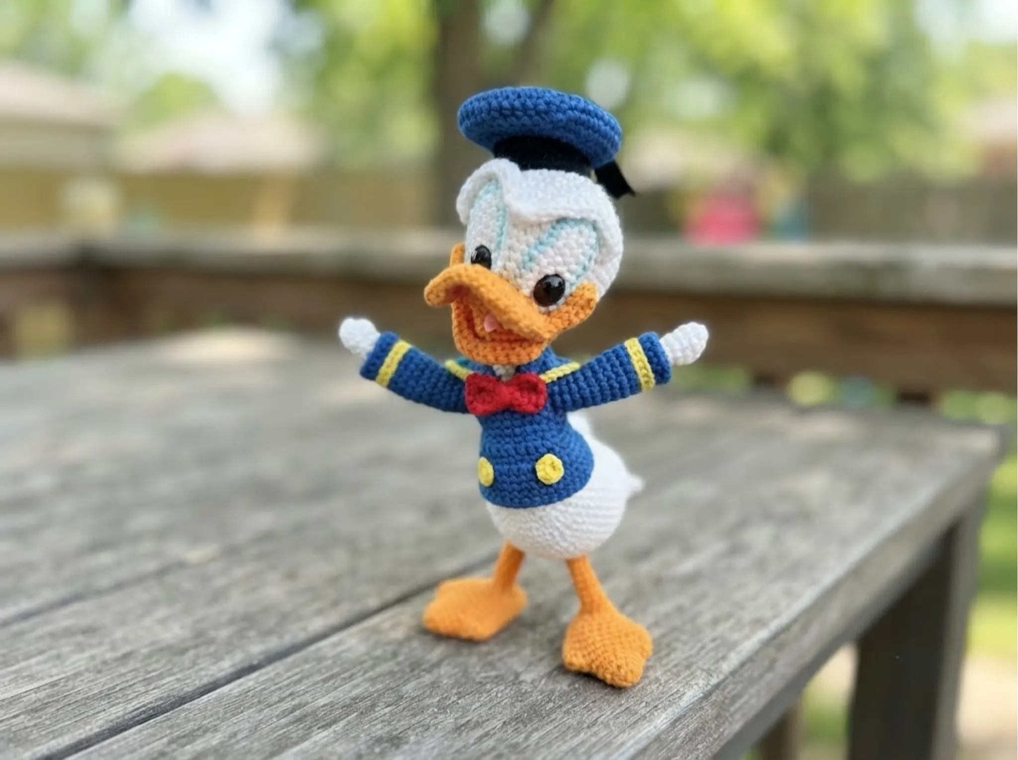 Crochet Duck in a Cap Amigurumi toy with white, blue, and orange yarn standing on a rustic wooden deck.