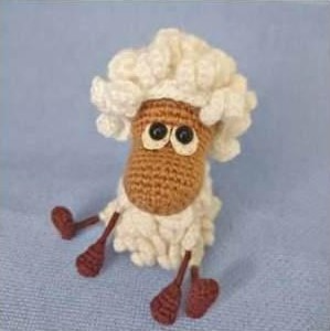 A completed curly sheep amigurumi toy with a fluffy cream white loop-stitch coat, a light brown face, glossy two-layer eyes, and thin poseable dark brown limbs sitting on a light blue background.