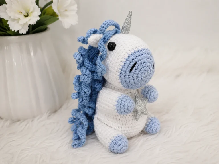 White and light blue yarn toy from this free unicorn amigurumi pattern sitting on white faux fur holding a silver star.