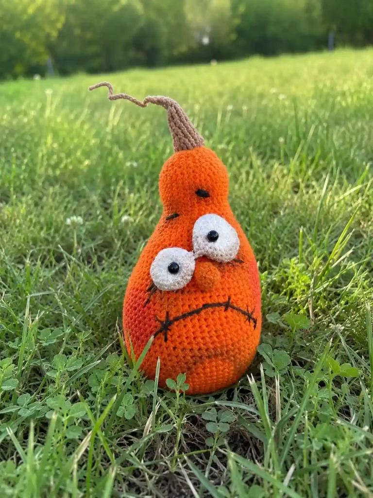 Orange crocheted ginger pumpkin amigurumi with a brown stem sitting in green grass