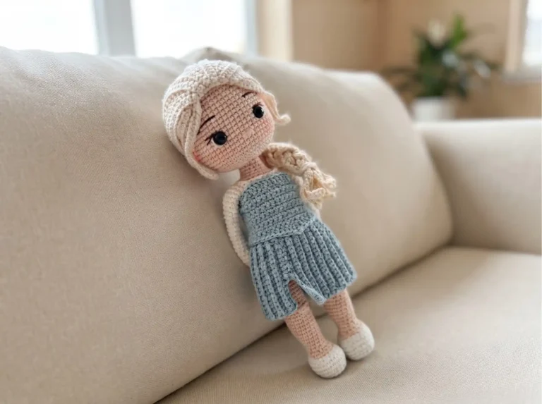 Crochet ice queen amigurumi with blonde braided hair and a blue dress resting on a beige sofa.