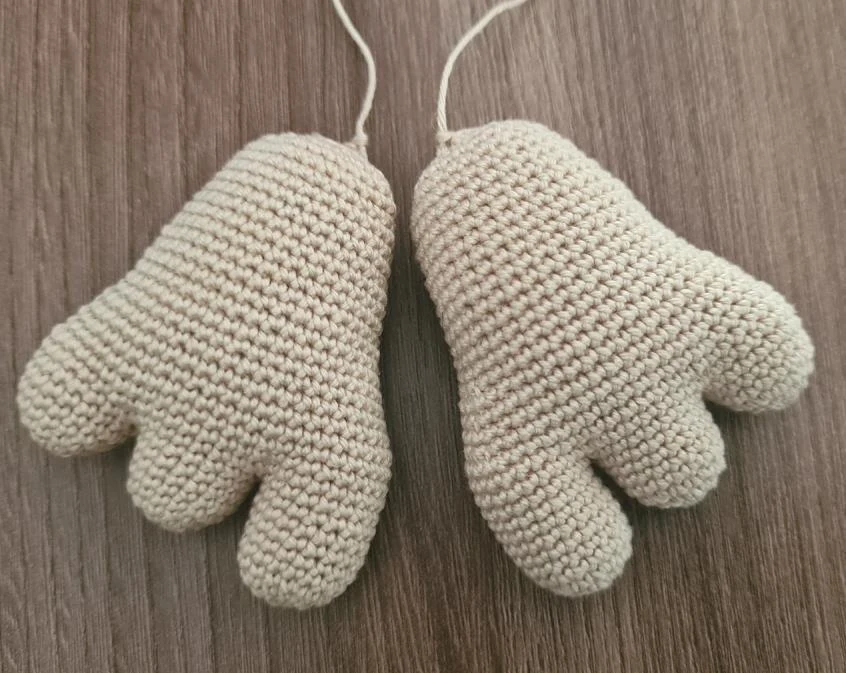 Two stuffed beige crocheted amigurumi feet, each with three distinct toes, resting side by side on a wooden surface with yarn tails extending from the tops.