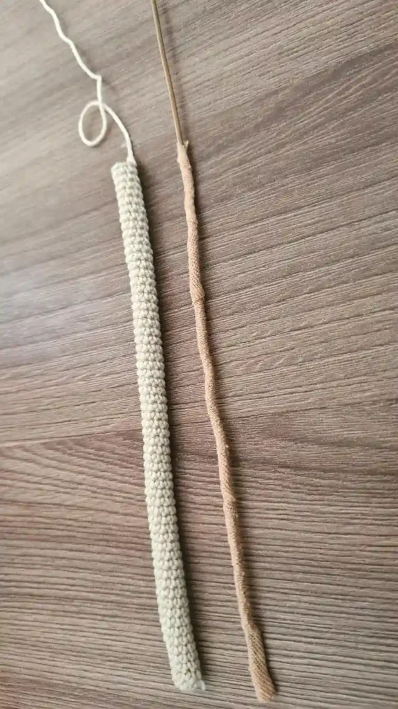 A long, thin beige crocheted tube lying on a wooden table next to a piece of craft wire partially wrapped in medical tape.