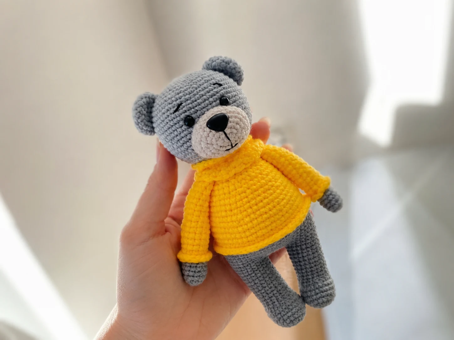 A gray crochet teddy bear wearing a ribbed yellow sweater and collar, sitting against a white background.