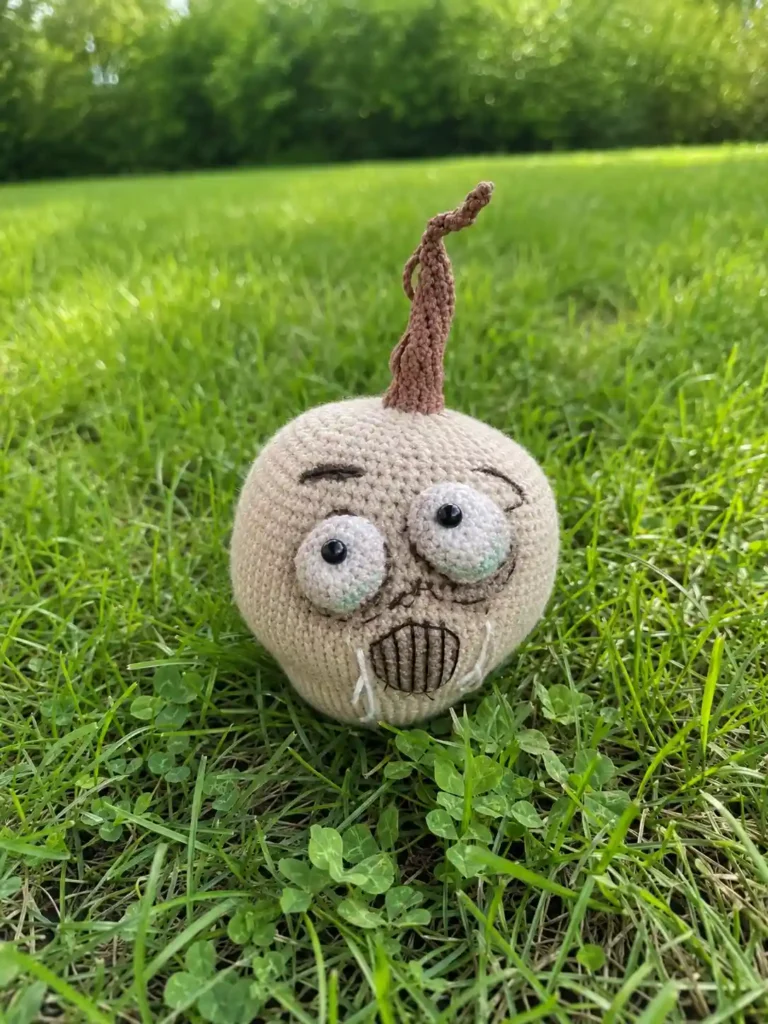 Off-white milk white crocheted pale pumpkin amigurumi with a tall brown stem sitting in green grass
