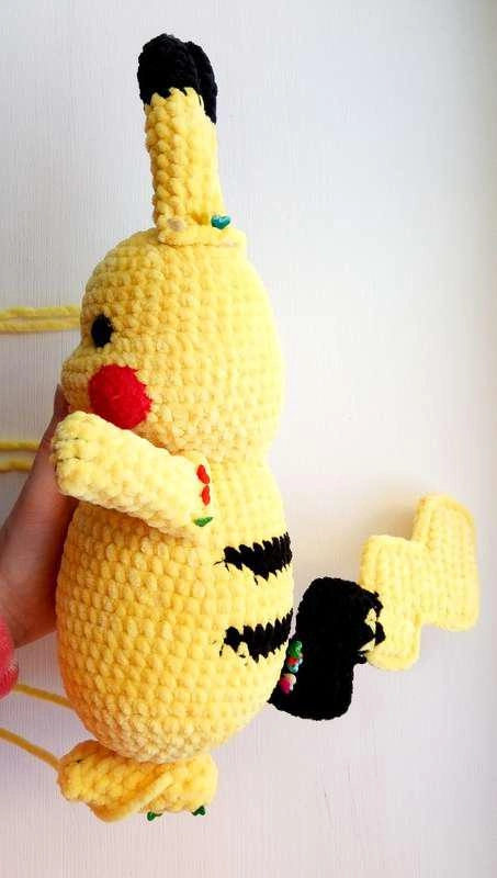 Side view of a finished crochet Pikachu amigurumi showing its yellow body, black back stripes, red cheek, and attached zigzag tail.