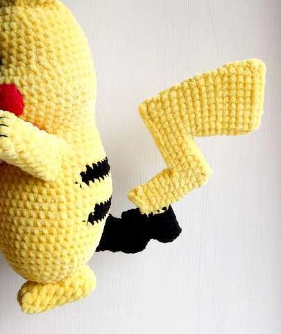 Close-up of a crocheted yellow and black zigzag tail attached to the lower back of a yellow Pikachu amigurumi plush.