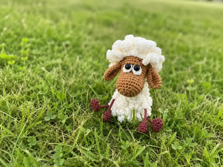 Crochet sheep amigurumi free pattern toy with white textured yarn wool and brown head sitting in green grass.