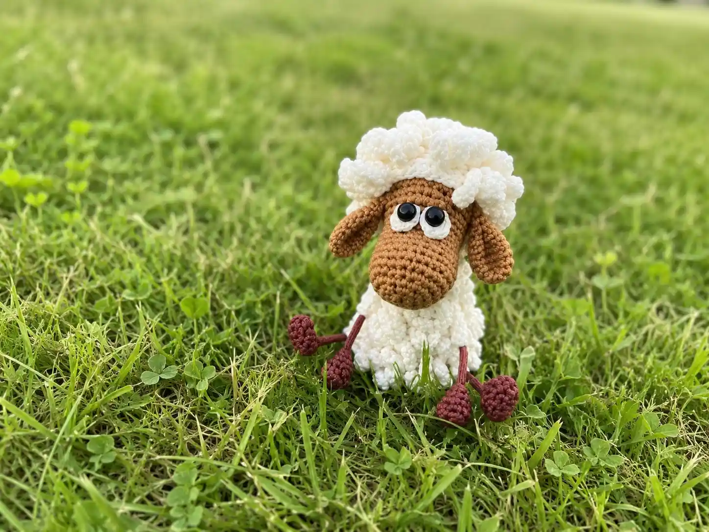 Crochet sheep amigurumi free pattern toy with white textured yarn wool and brown head sitting in green grass.