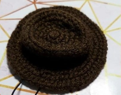A top-down view of a small, warm brown crocheted cowboy hat designed for a Sheriff Woody amigurumi doll, showing a round crown and a wide brim.
