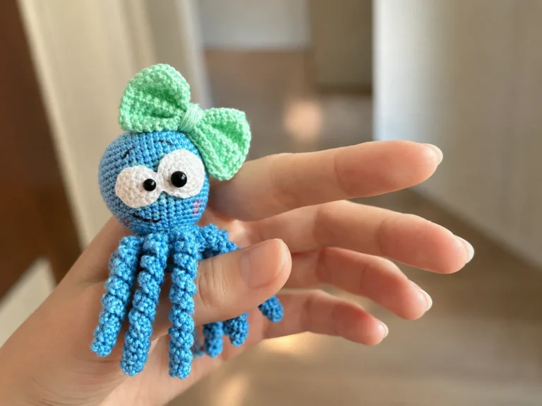 Person holding small blue amigurumi octopus with mint green bow and large eyes, using the free octopus amigurumi pattern.