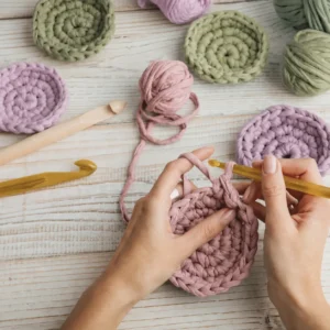 Hands crocheting a dusty pink circle surrounded by colorful yarn and crochet hooks.