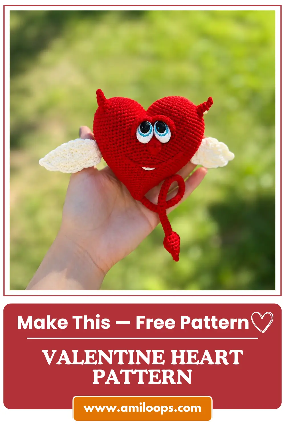 Hand holds a red yarn toy from our crochet valentine heart free pattern with white wings against a green nature backdrop.