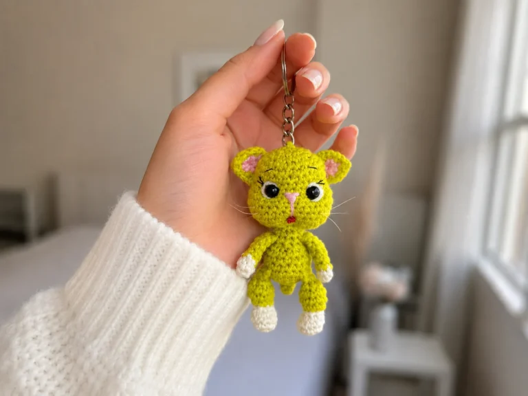 A lime-green crochet avocado cat amigurumi keychain with pink ears, held up by a silver keyring.