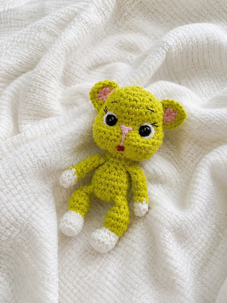 Green crocheted kitten from our avocado cat amigurumi pattern resting on a white textured knitted blanket.