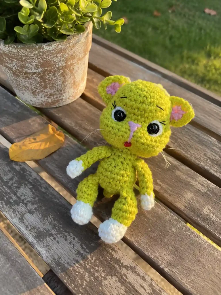 Green avocado cat amigurumi pattern finished toy sitting on a wooden slatted table outdoors in warm sunlight.