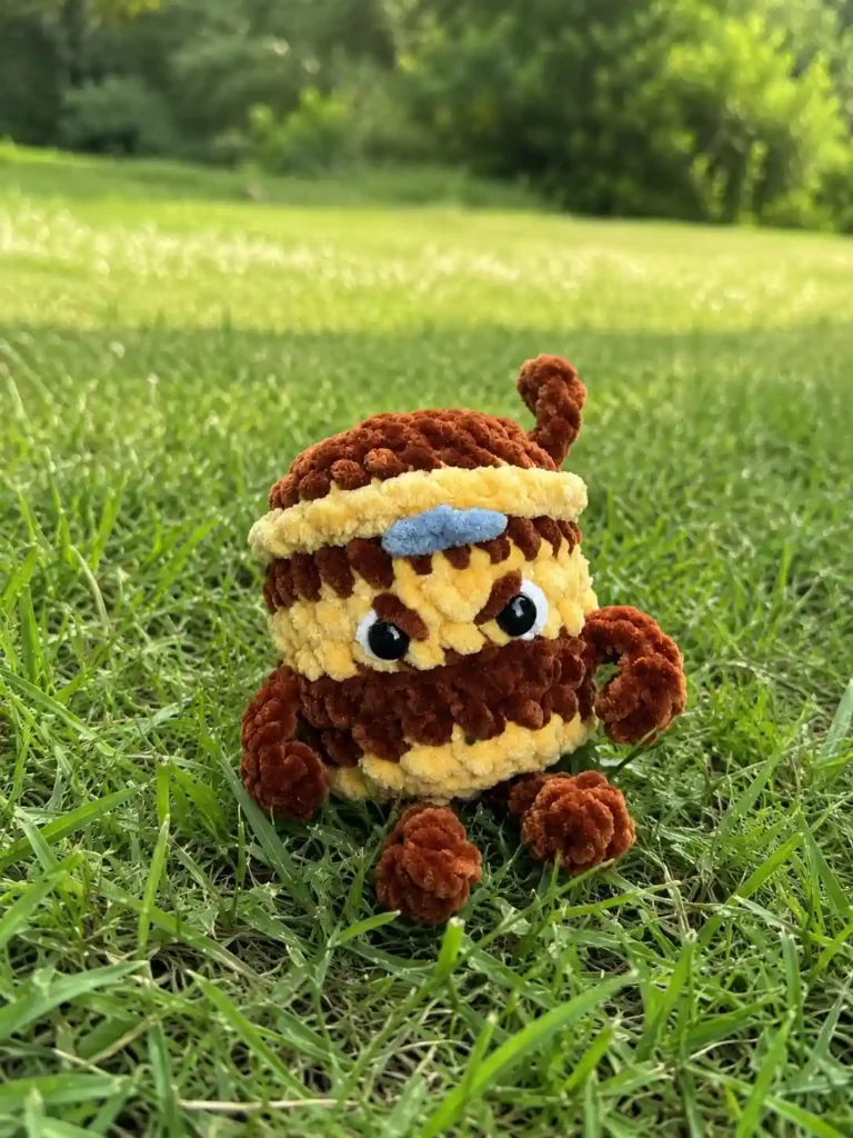 Brown and beige chenille ninja cup from this cappuccino assassino crochet pattern free sitting outdoors in green grass.