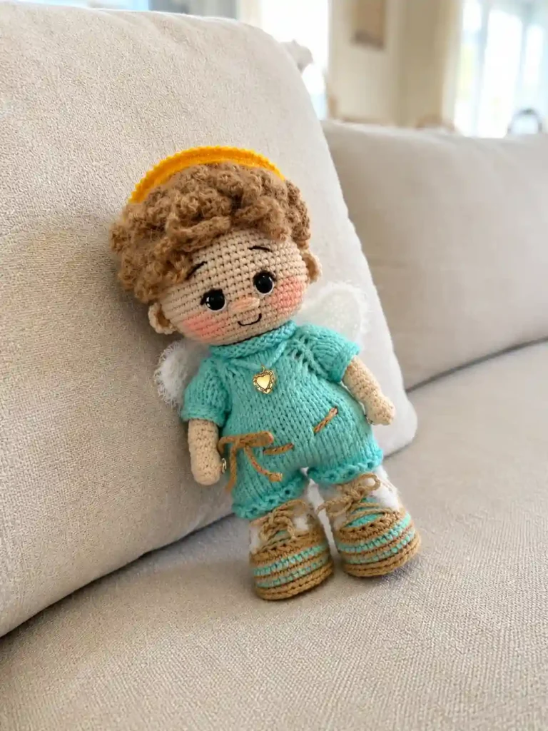 A crochet angel baby doll amigurumi pattern free resting on a beige couch, showing a yellow halo and tan lace booties.