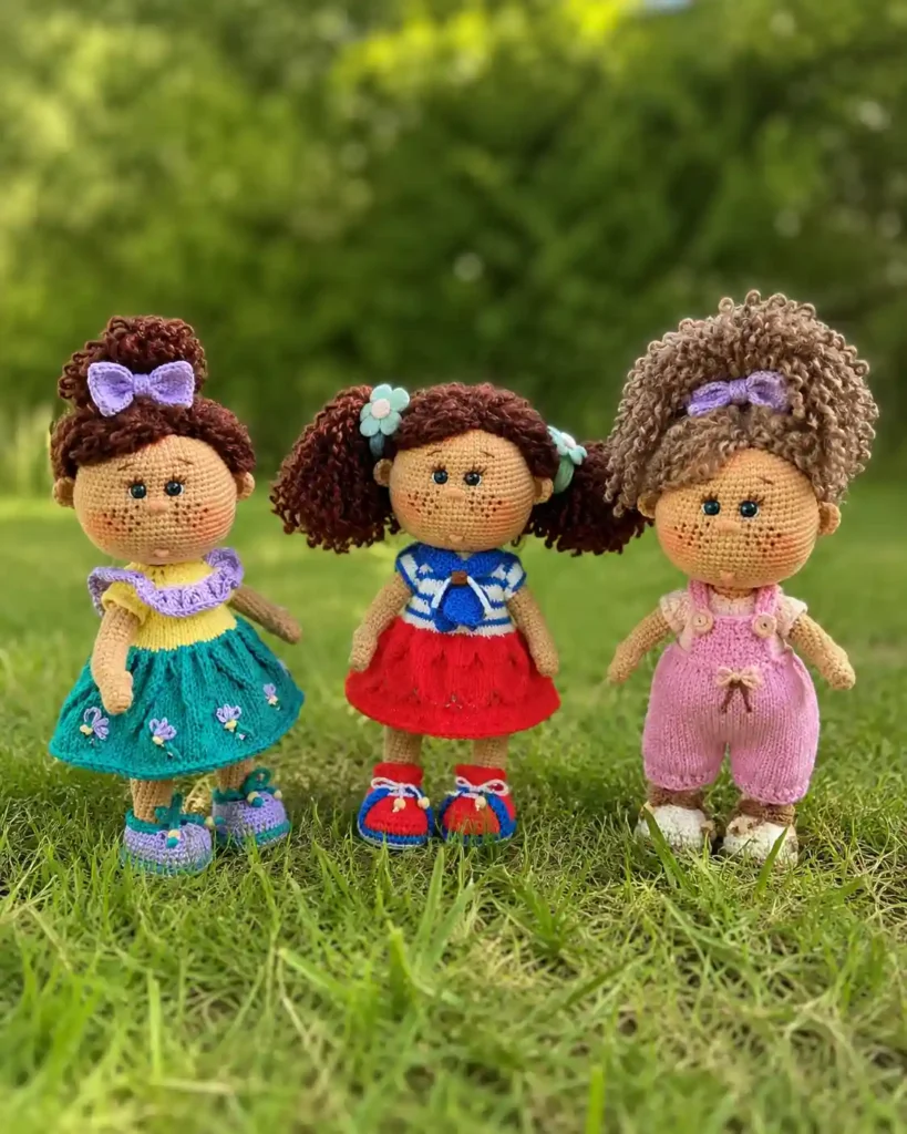 Three handmade dolls in teal, red, and pink standing on green grass wearing a crochet boucle yarn wig free pattern.