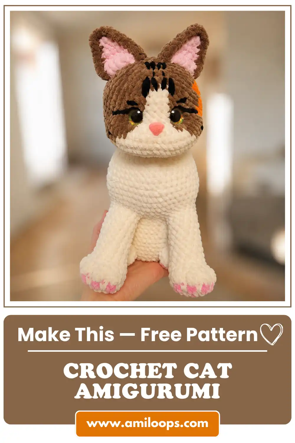 A hand holding a cute crochet cat amigurumi free pattern made of plush brown and white yarn in a sunny room.