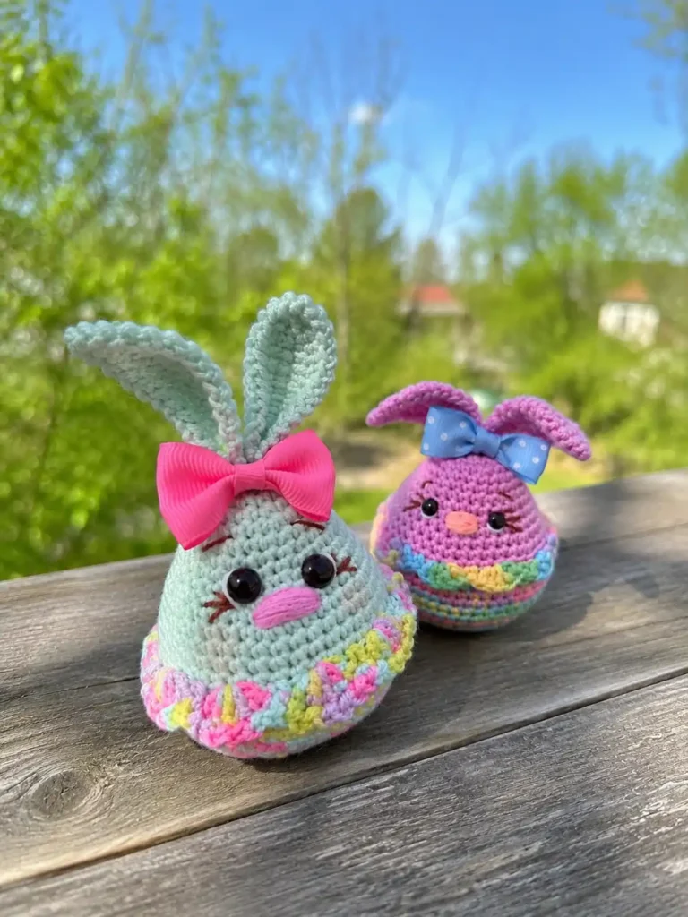 Free crochet Easter bunny amigurumi pair in mint green and pink pastel yarn with melange skirts, bows, and embroidered facial details sitting outdoors on a wooden surface.