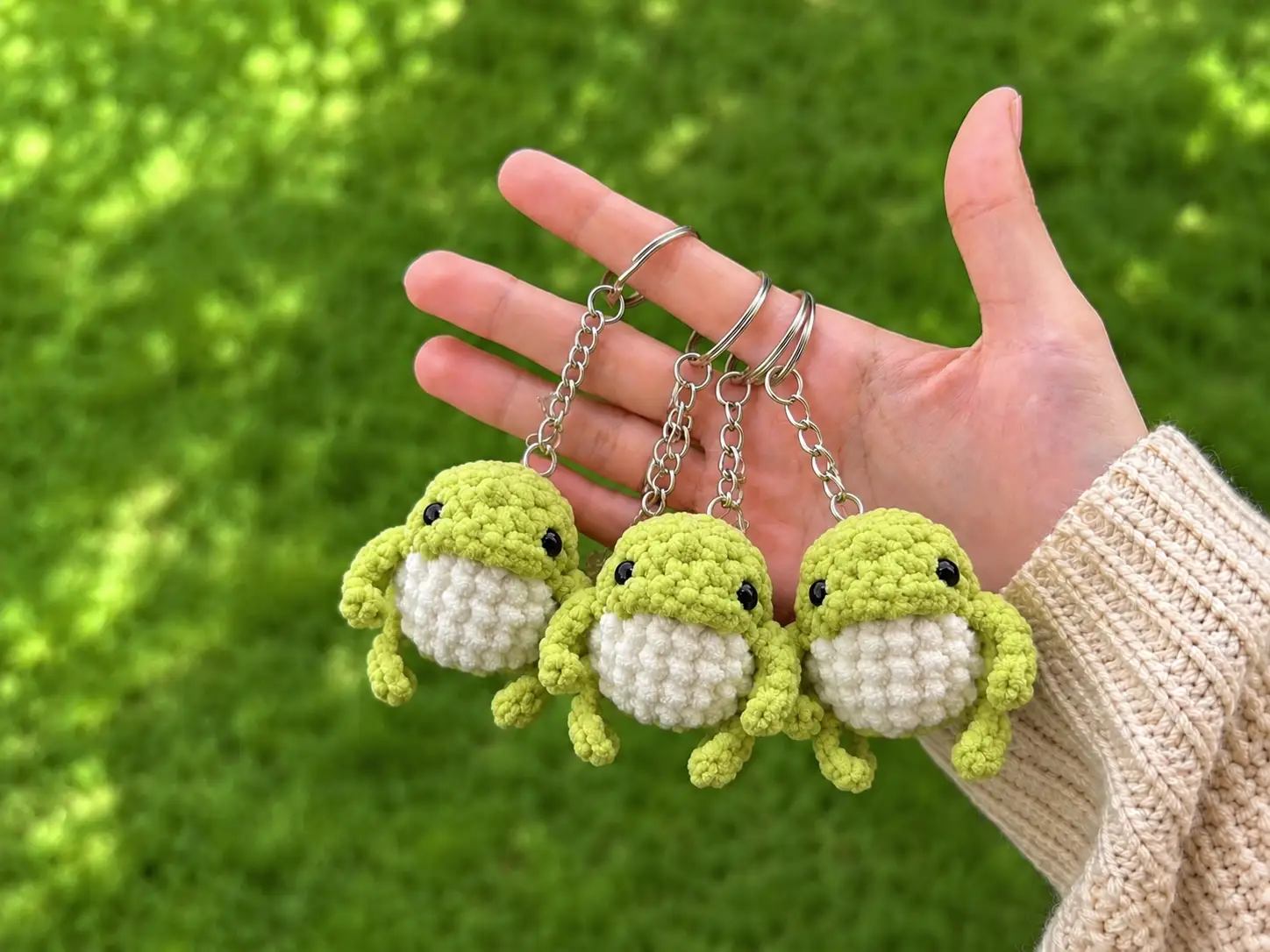 A velvety green and white crochet frog amigurumi keychain with black stitched mouth and safety eyes.