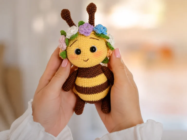 A yellow and brown striped crochet bee amigurumi with a floral crown lying in green grass outdoors.