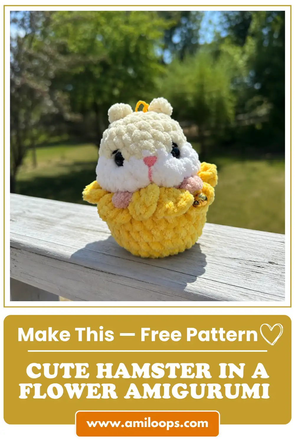 Plush cream and white hamster in a flower amigurumi pattern sitting on a white wooden railing outdoors with green trees.