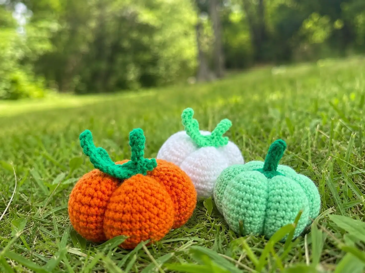 A small orange crochet pumpkin amigurumi with a green stem and curled leaf on a white background.