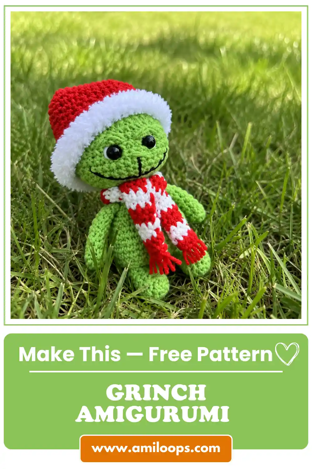 Green grinch amigurumi free crochet toy with a fluffy red Santa hat and striped scarf sitting in bright green grass.