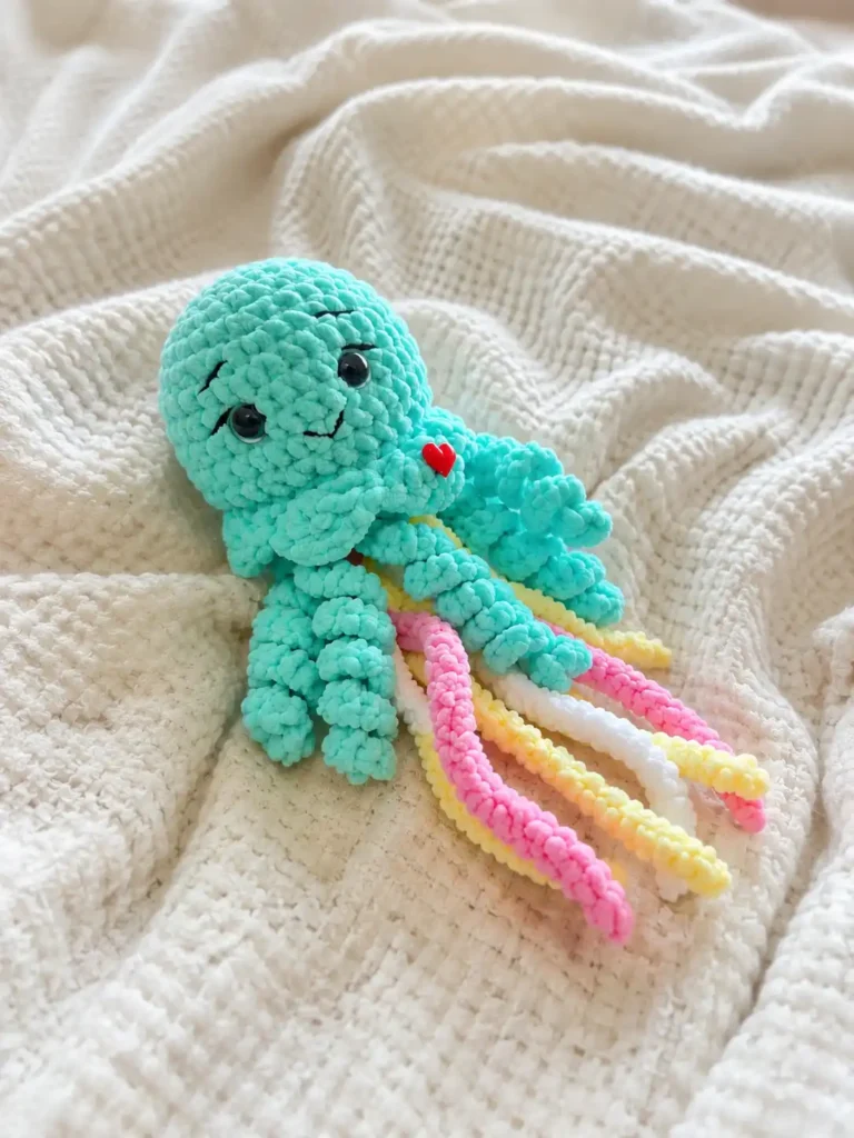Mint green jellyfish amigurumi free pattern placed diagonally on a soft white waffle texture blanket.