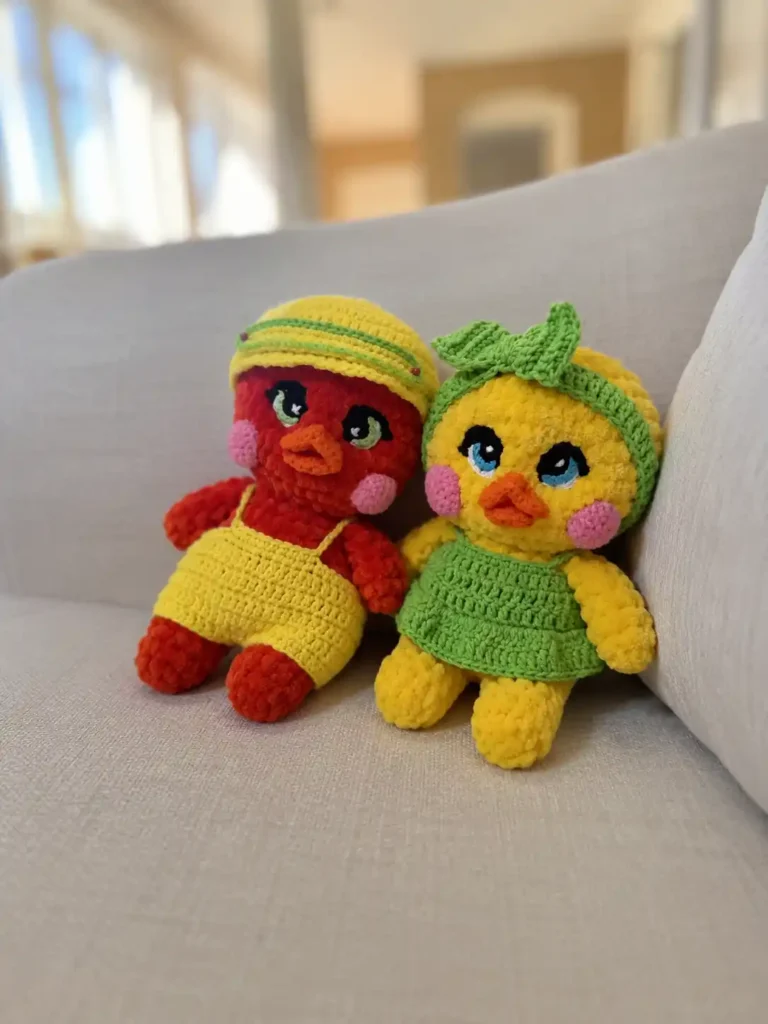 Red and yellow chenille amigurumi ducks sit on a beige couch for the Lulu the duck and Lolo the drake free crochet pattern.