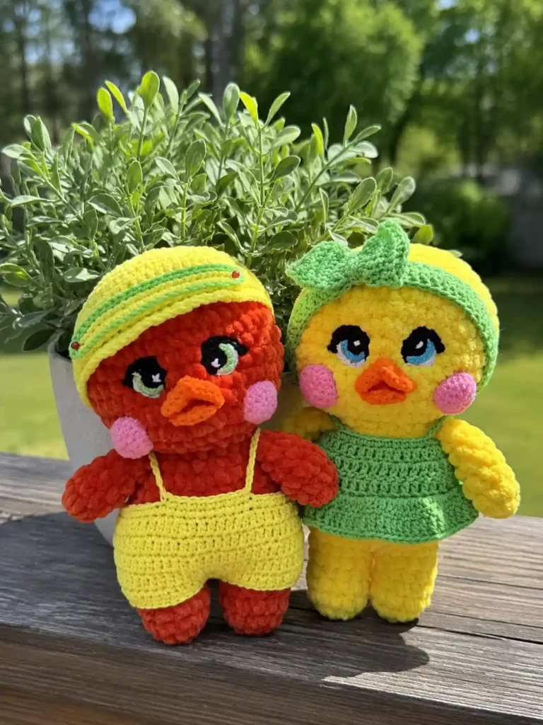 Chenille toys for the Lulu the duck and Lolo the drake free crochet pattern stand on a wood deck by a potted green plant.