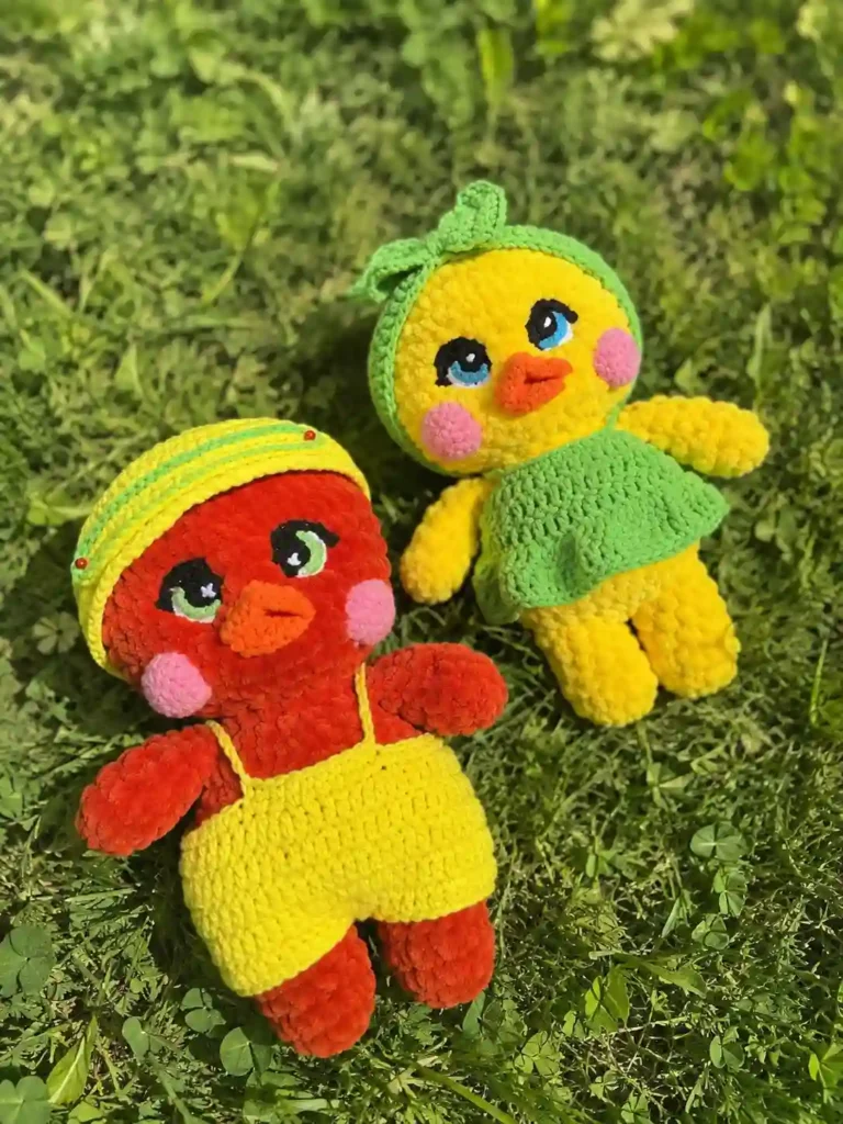 Red and yellow chenille ducks lie on green grass outdoors in this Lulu the duck and Lolo the drake free crochet pattern.
