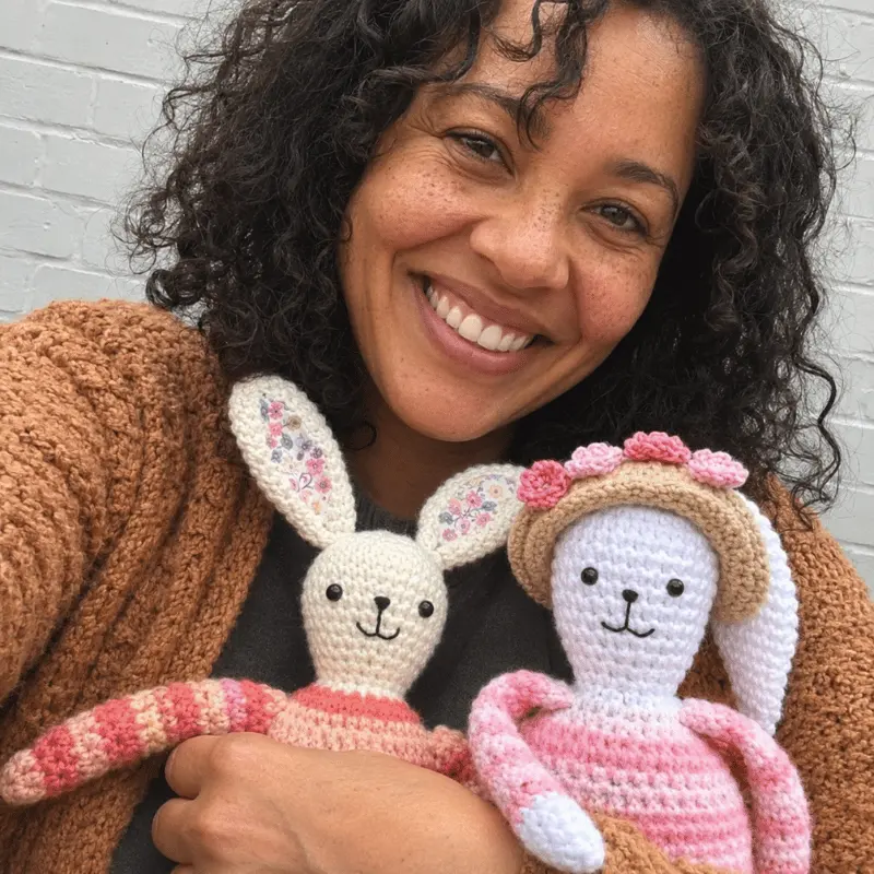 Mia from AmiLoops holding two handmade crochet bunny dolls in pink and neutral colors.
