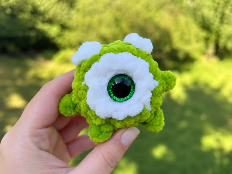 A green crochet monster amigurumi held in a hand outdoors, with a row of finished monster plushies lined up on a couch.