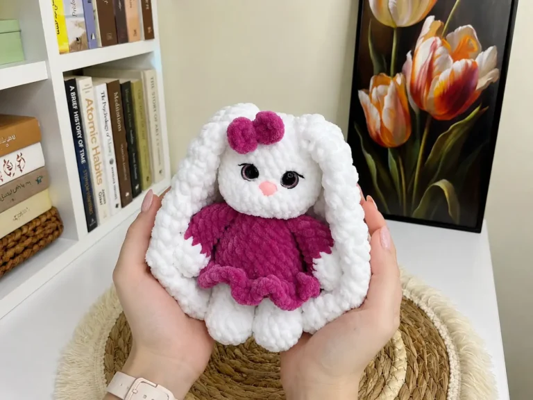 A plush chenille amigurumi bunny with a pink skirt and bow, made from scrap yarn, on a white background.