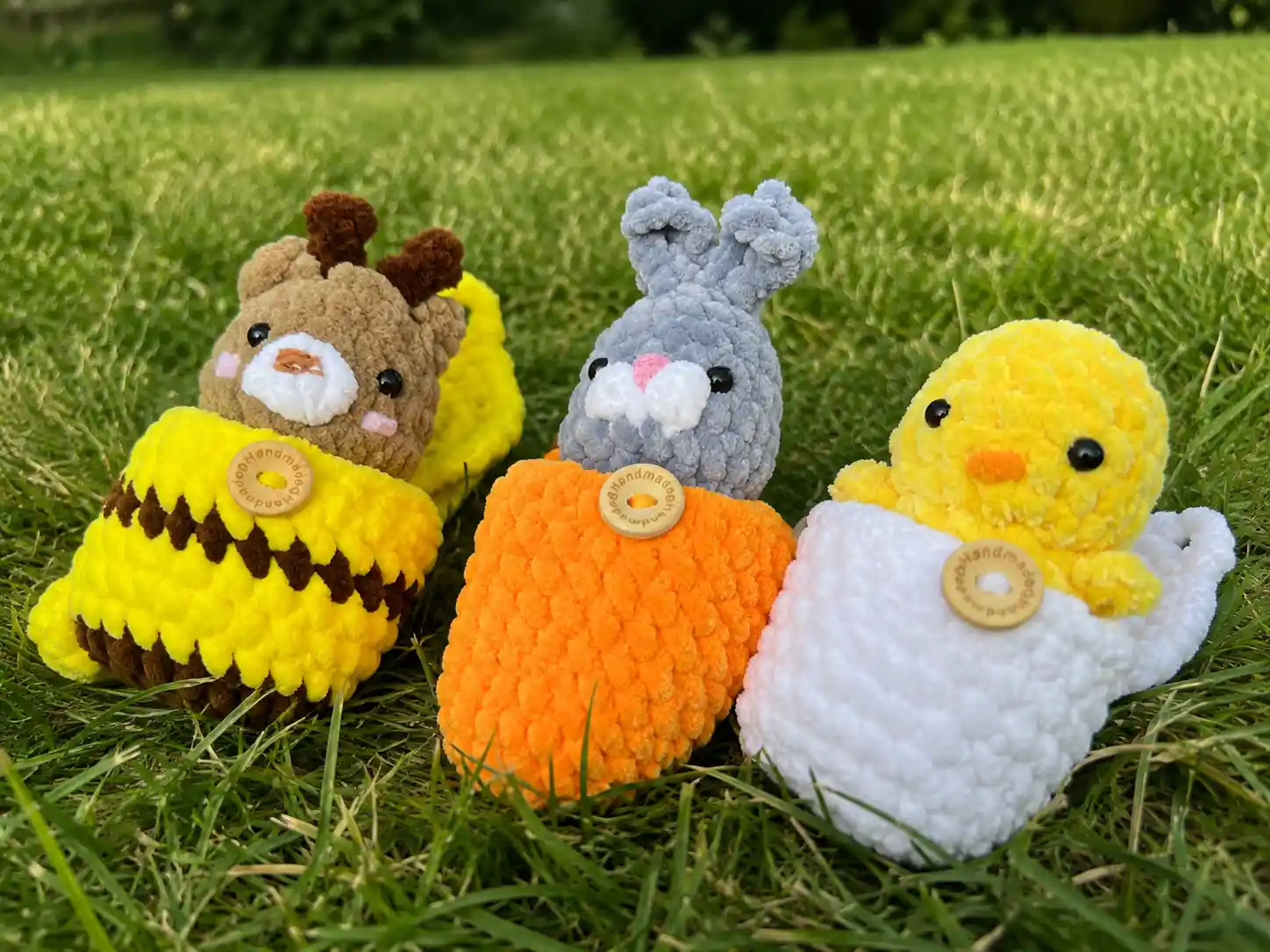 Hands holding three mini crochet animal eggs — a bee, bunny, and duckling in soft chenille pouches.